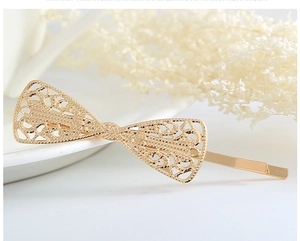 Detail of golden lace hollow bow hairpin made of alloy on a white ceramic plate