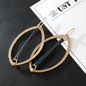 Detail view of a golden metal leaf-shaped hair clip with black textured bar decoration