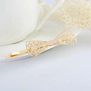 Elegant gold hollow bow hair clip with lace pattern on white porcelain plate
