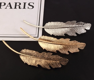 Macro detail of three metallic feather hair clips in silver, gold, and bronze finishes