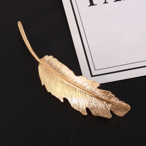 Elegant gold feather hair clip with intricate metallic texture on a minimalist black background