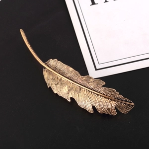 Detailed close-up of retro golden feather hair clip with fine brushed alloy texture