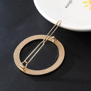 Close-up of golden circular hair clip with radiant texture and pin on black background