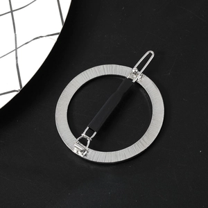 Detail of silver round hair clip featuring a brushed metal texture and black securing bar