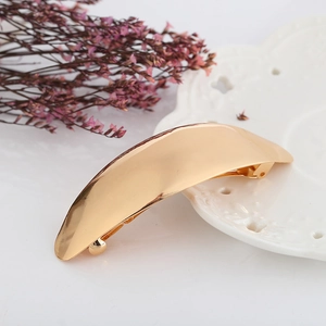 Polished golden metal hair clip with a curved minimalist design on a white ceramic plate
