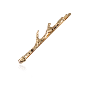 Detail of golden twig shaped hair clip with textured branch design and metallic finish