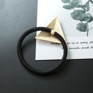 Detail of matte gold triangle charm on black elastic hair tie with brushed metal finish