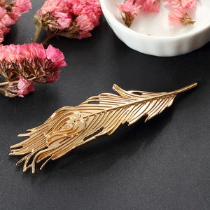 Elegant gold feather hair clip with heart details on a dark background with pink flowers