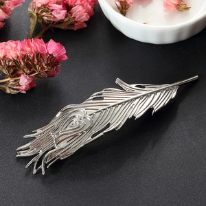 Elegant silver feather hair clip with heart detail on a textured black surface