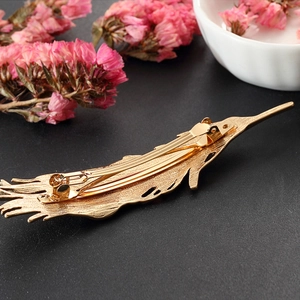 Golden phoenix tail feather hair clip with intricate textures and spring closure