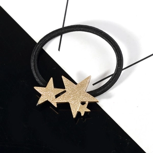 Elastic black hair tie with three textured gold stars on a minimalist background