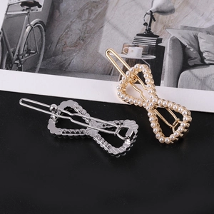Détail du set barrette perle dorée et nœud strass argenté sur un fond noir élégant
