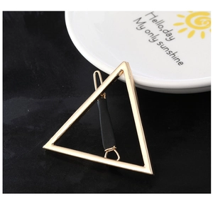 Détail d'une pince à cheveux triangulaire dorée minimaliste sur un fond noir texturé