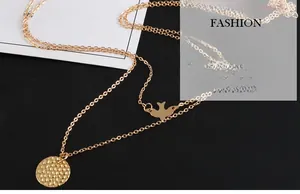 Detailed close-up of double-layer gold necklace featuring a bird charm and round pendant