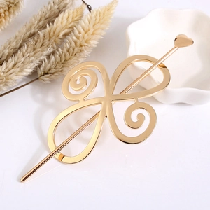 Detail of elegant gold hollow metal hair pin with heart ornament and spiral patterns