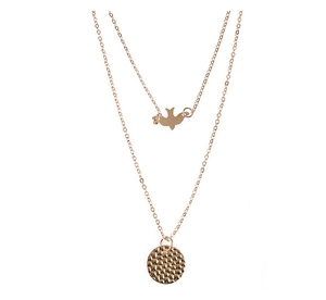 Detail of double-layer gold necklace featuring bird charm and hammered round pendant