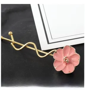 Dettaglio del fermaglio per capelli dorato ondulato con un fiore in smalto rosa lucido