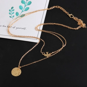 Double-layered gold necklace with bird and hammered disc pendants on black background