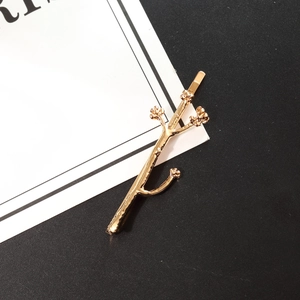 Elegant golden branch hair clip with small flower accents on a minimalist background