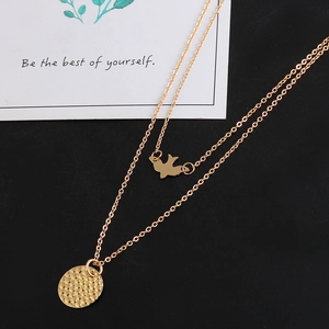 Layered gold necklace featuring bird and hammered disc pendants on black background