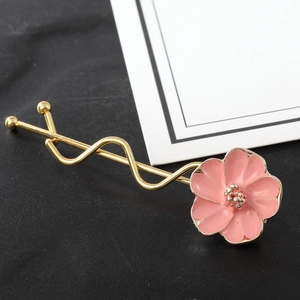 Fermaglio dorato minimalista con fiore in smalto rosa su sfondo scuro testurizzato