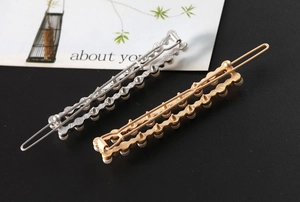 Détail de barrettes rectangulaires en métal doré et argenté avec perles sur fond noir