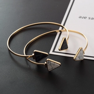 Detail of gold open bangles with marble textured triangle ends on black background