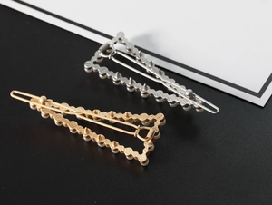 Detail of gold and silver triangle hair clips with white faux pearls on black surface