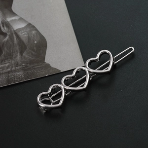 Macro shot of silver alloy hair clip featuring three hollow heart patterns on dark background