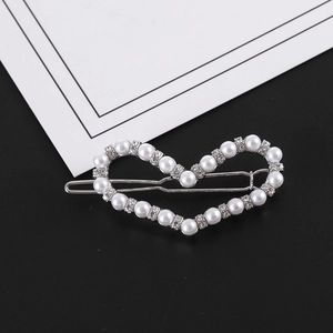 Détail de la pince à cheveux en cœur avec perles et strass sur un fond noir élégant