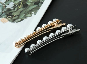 Detalle de pinzas doradas y plateadas con perlas y grabado Korea sobre el metal