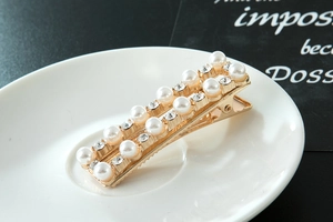 Detail van gouden rechthoekige haarclip met dubbele rij parels en schitterende strass-steentjes