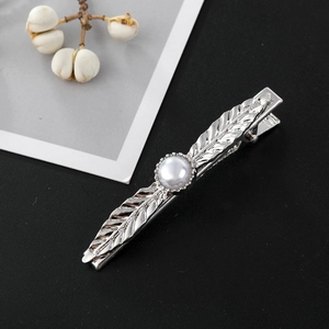 Detail of silver leaf hair clip with a centered pearl on a dark textured background