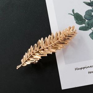 Vintage golden metal feather leaf hair clip with detailed texture on a black background