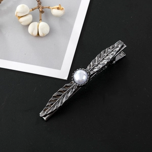 Detailed close-up of a vintage leaf-shaped hair clip with a pearl on black background