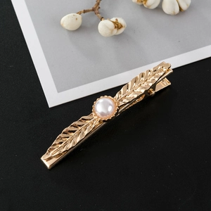 Close-up of golden leaf hair clip with white pearl detail on minimalist display card