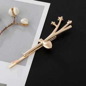 Detail of golden branch-shaped hair clip with star accents on minimalist dark background