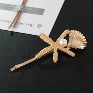 Eleganter goldener Seestern und Muschel Haarklammer mit Perle auf glattem schwarzem Grund