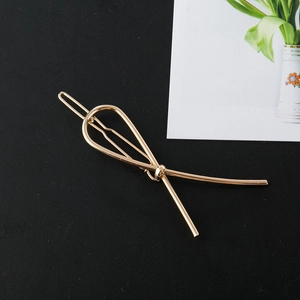 Minimalist golden metal bow hairpin with a twisted knot design on a black background