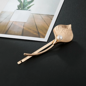 Macro detail of tulip hair clip with brushed gold texture and elegant white pearl accent