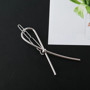 Close-up of a silver polished metal hair clip with a minimalist crossed-line bow design