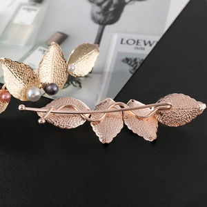 Macro shot of gold leaf hair clips featuring pearl accents and textured metal finish