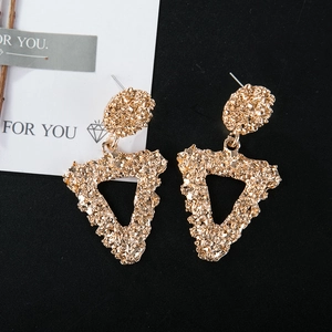 Detailed close-up of golden triangular drop earrings with unique hammered metal texture