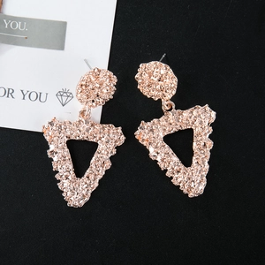 Macro detail of large rose gold geometric triangle earrings with hammered metal texture