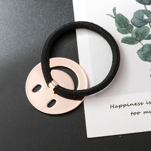 Gros plan sur un élastique noir avec un pendentif visage souriant en métal brossé or rose