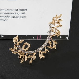 Detailed close-up of golden leaf ear cuff with sparkling rhinestones in a luxury nature style
