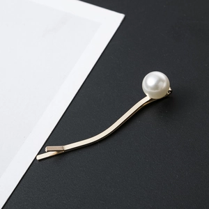 Macro shot of gold curved hair clip with pearl detail against a minimalist background
