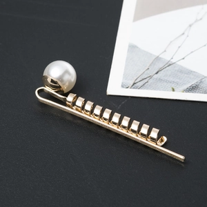 Elegant gold metal twist hair clip featuring a large white pearl on a dark textured surface