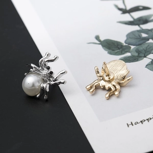 Silver and gold spider earrings with white pearls and black gemstones on a display card