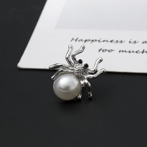 Detailed view of silver spider brooch featuring a large white pearl and black crystal eyes
